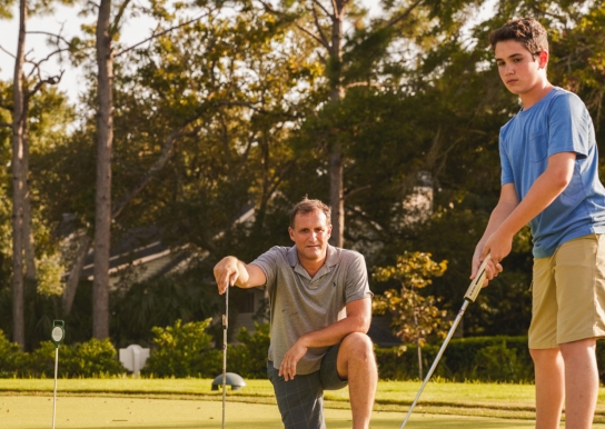 Father watching son putt on the putting green at 78Fitness