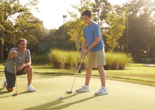 Father and son on putting green and the son is about to take his shot