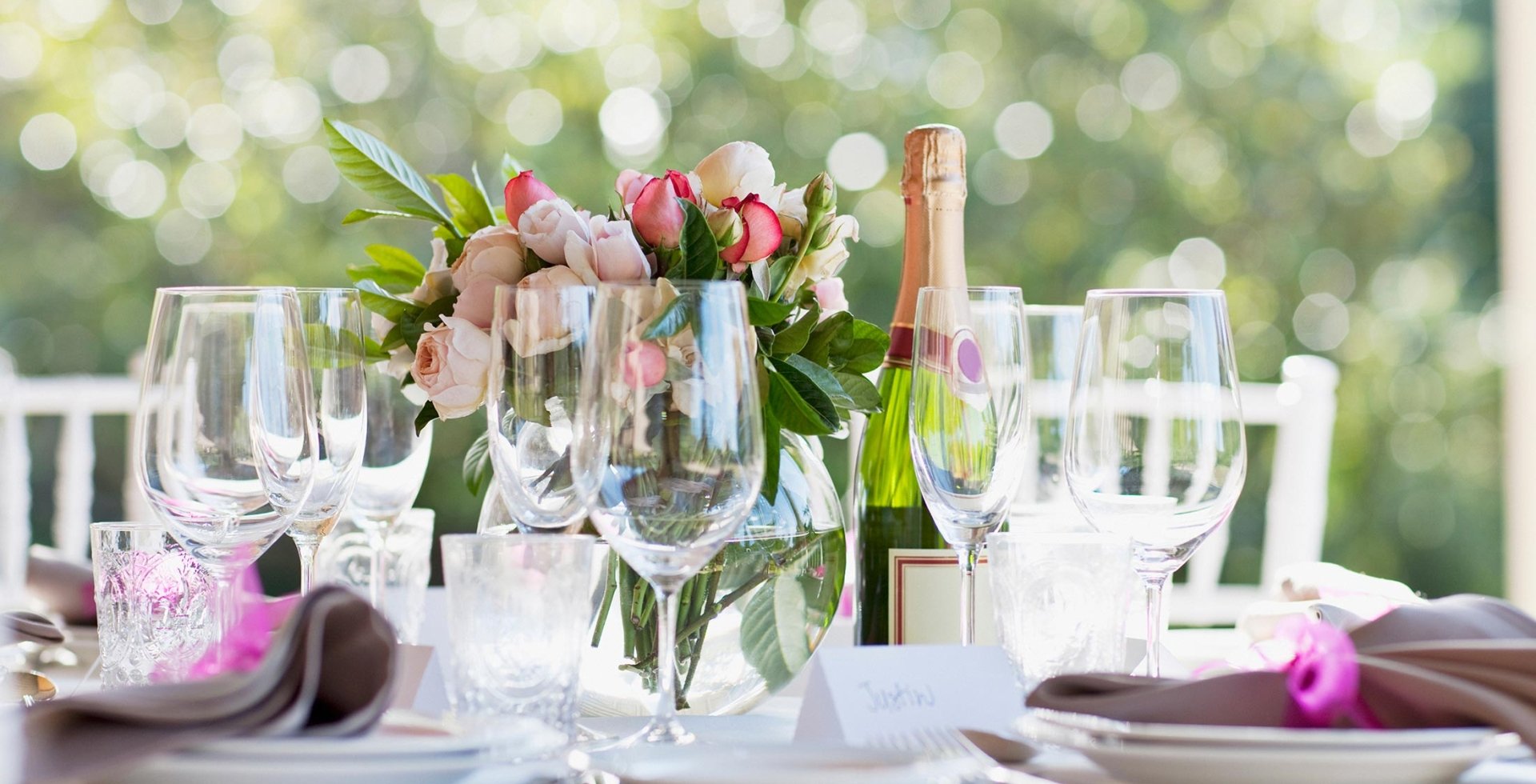 Table set for wedding with wine and champagne glasses, pink roses centerpiece, and a bottle of wine