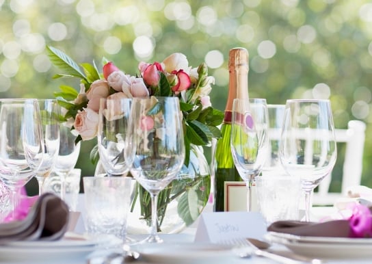 Table set for wedding with wine and champagne glasses, pink roses centerpiece, and a bottle of wine