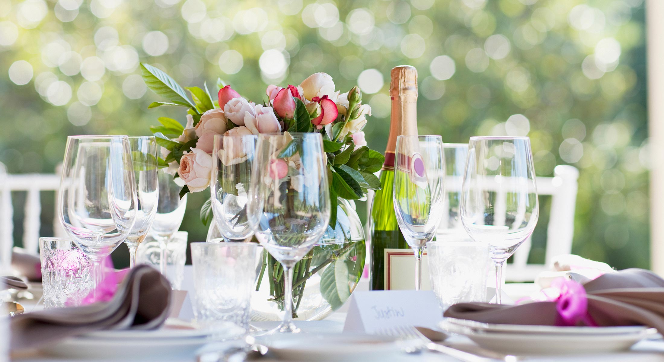 Table set for wedding with wine and champagne glasses, pink roses centerpiece, and a bottle of wine