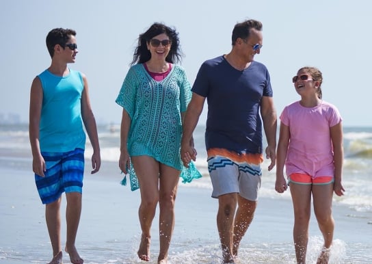 Happy family walking on the beach with their feet in the ocean