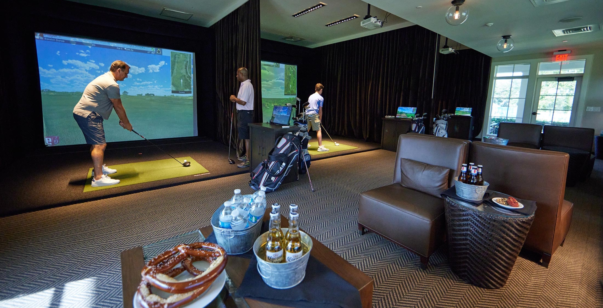 Men playing the Golf simulators at The Landing with buckets of beer, and water, and snacks such as pretzels and cookies