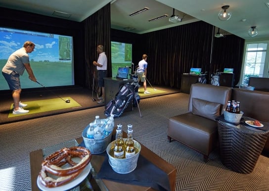 Men playing the Golf simulators at The Landing with buckets of beer, and water, and snacks such as pretzels and cookies