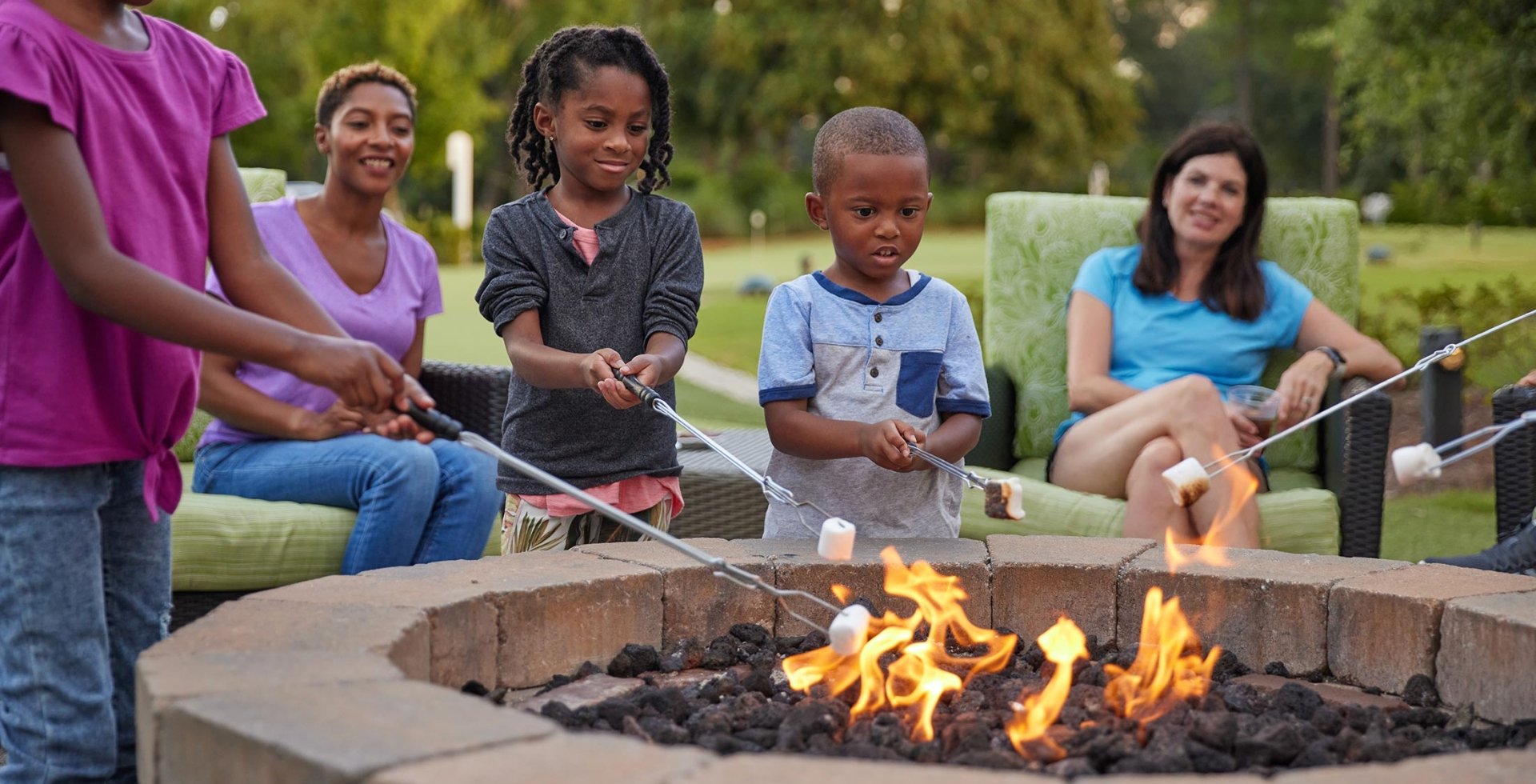 Kids roasting marshmallows and two moms sitting behind them