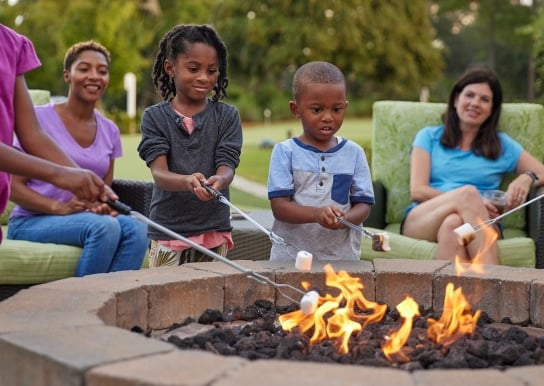 Kids roasting marshmallows and two moms sitting behind them