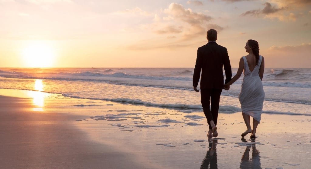 Bride and groom walking on beach at sunset