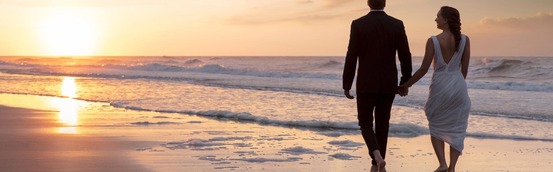 Bride and groom walking on beach at sunset