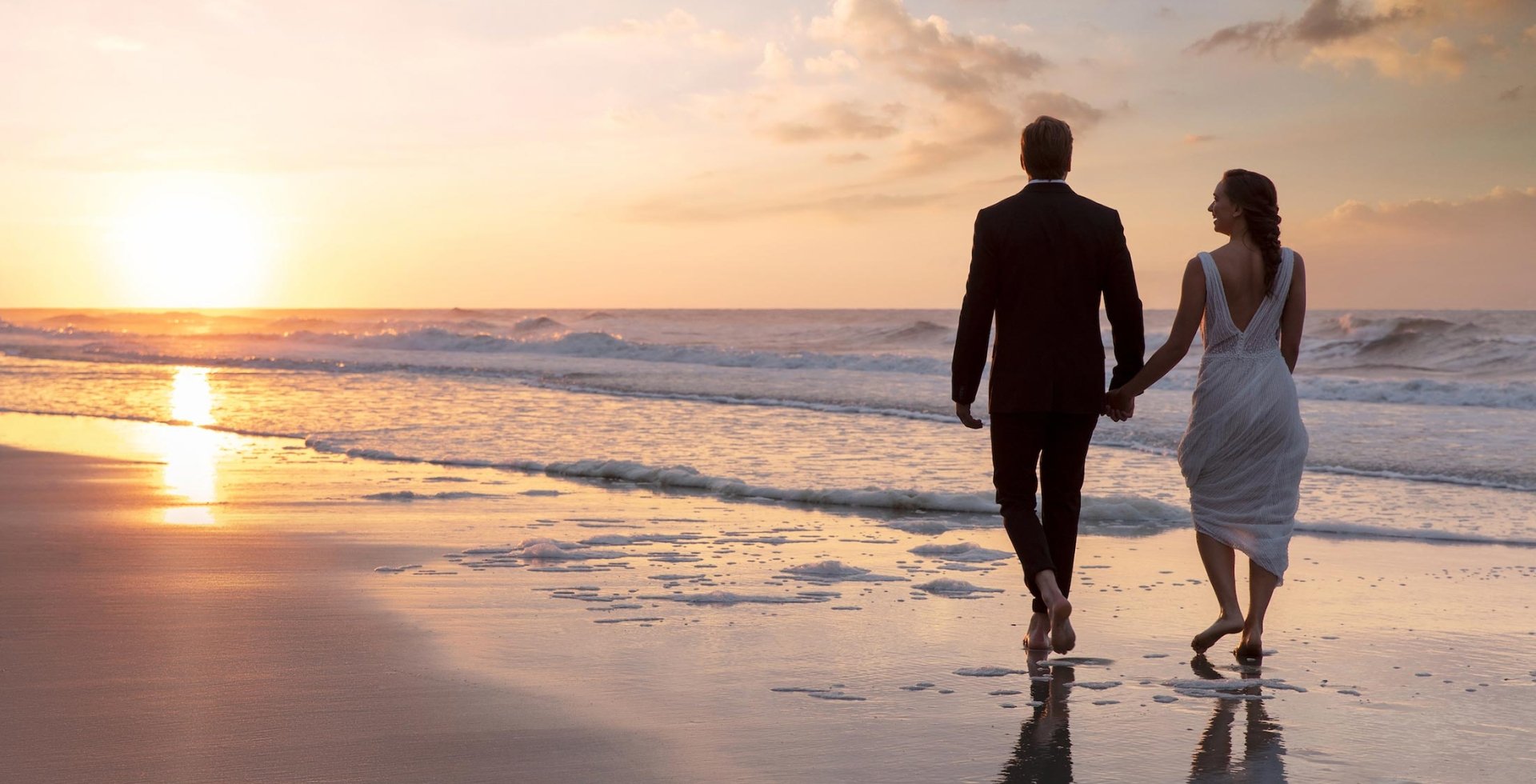 Bride and groom walking on beach at sunset