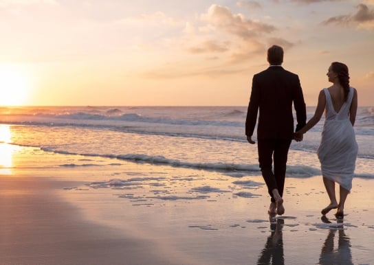 Bride and groom walking on beach at sunset