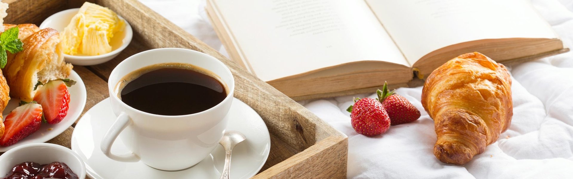 Breakfast in bed with a book. Coffee, croissants with jam and butter, and fresh strawberries