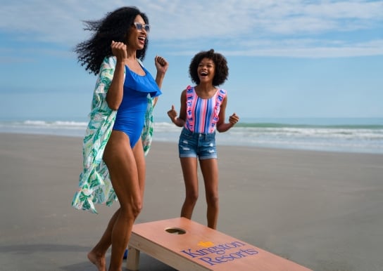 Mom and daughter jumping up and down in excitement playing cornhole on the beach