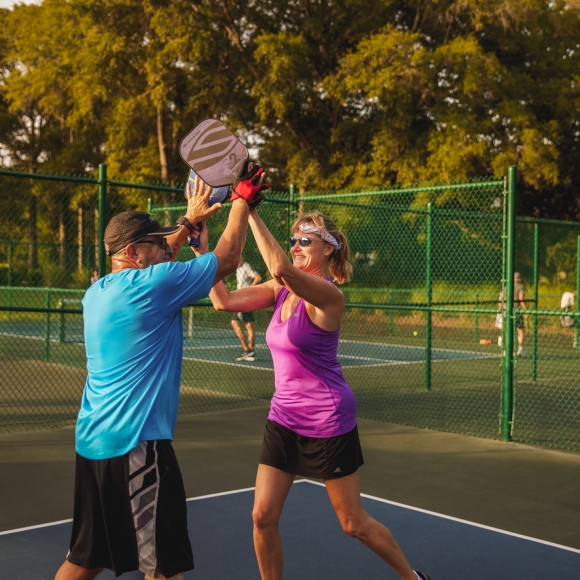 Two people high five on a pickleball court
