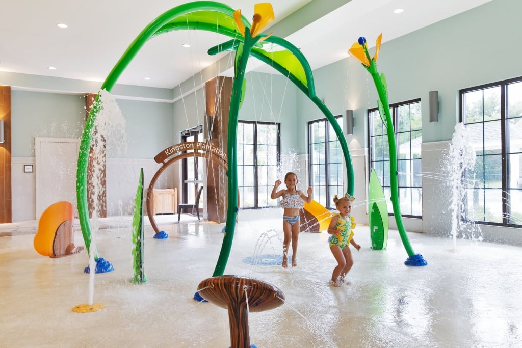 Two girls splash in the water of an indoor sprinkler.