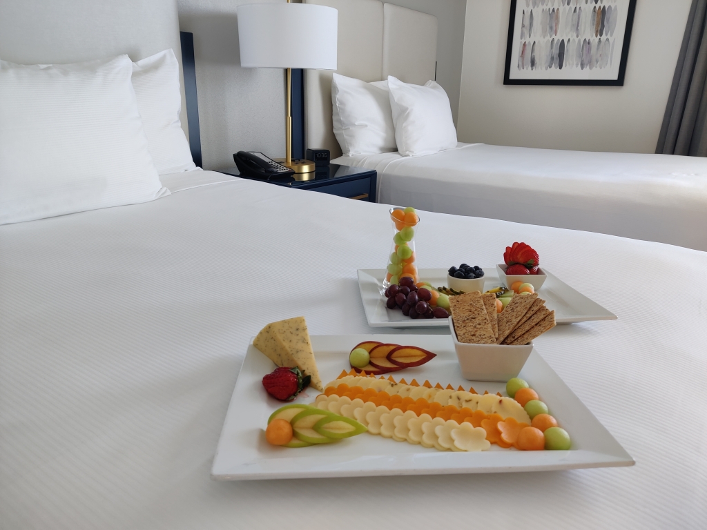 A platter of fruit and cheeses lays on a bed in a hotel room