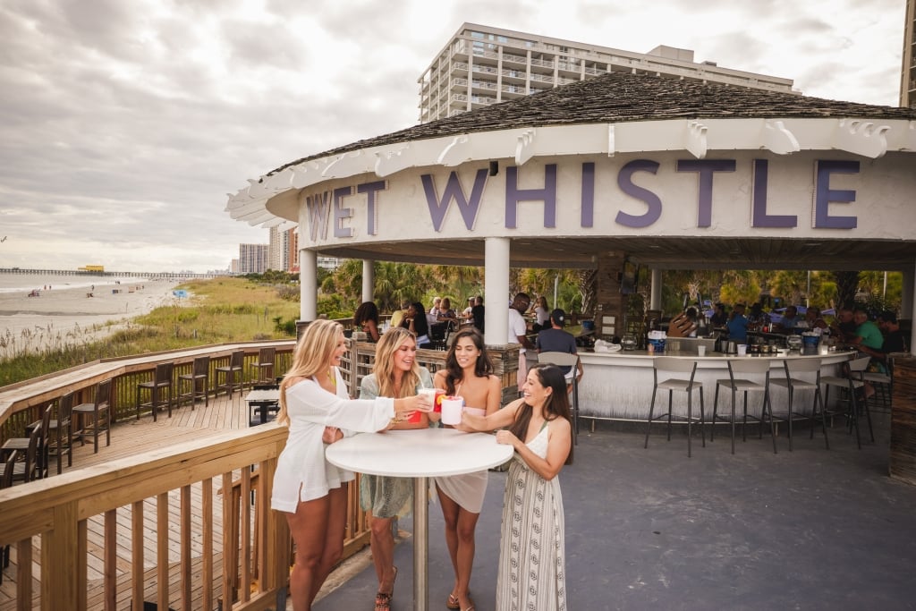 Four girls stand around a bar table cheersing drinks