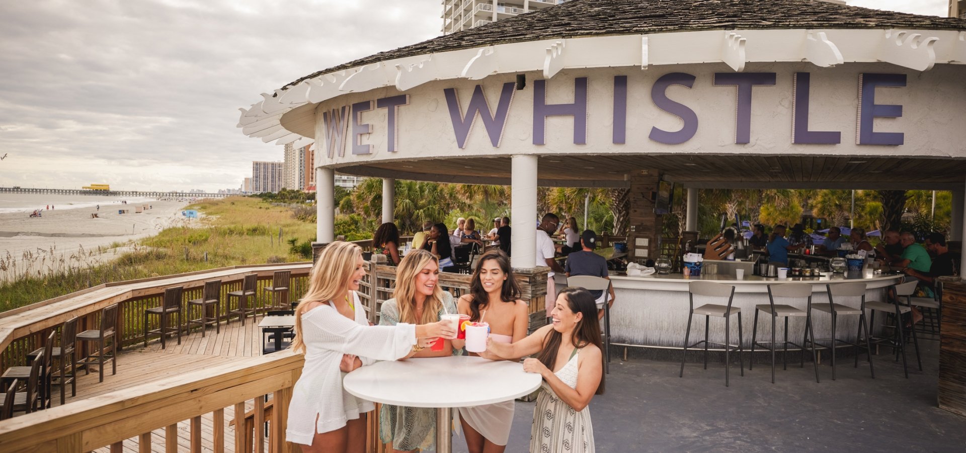 Four girls stand around a Wet Whistle bar table cheering drinks