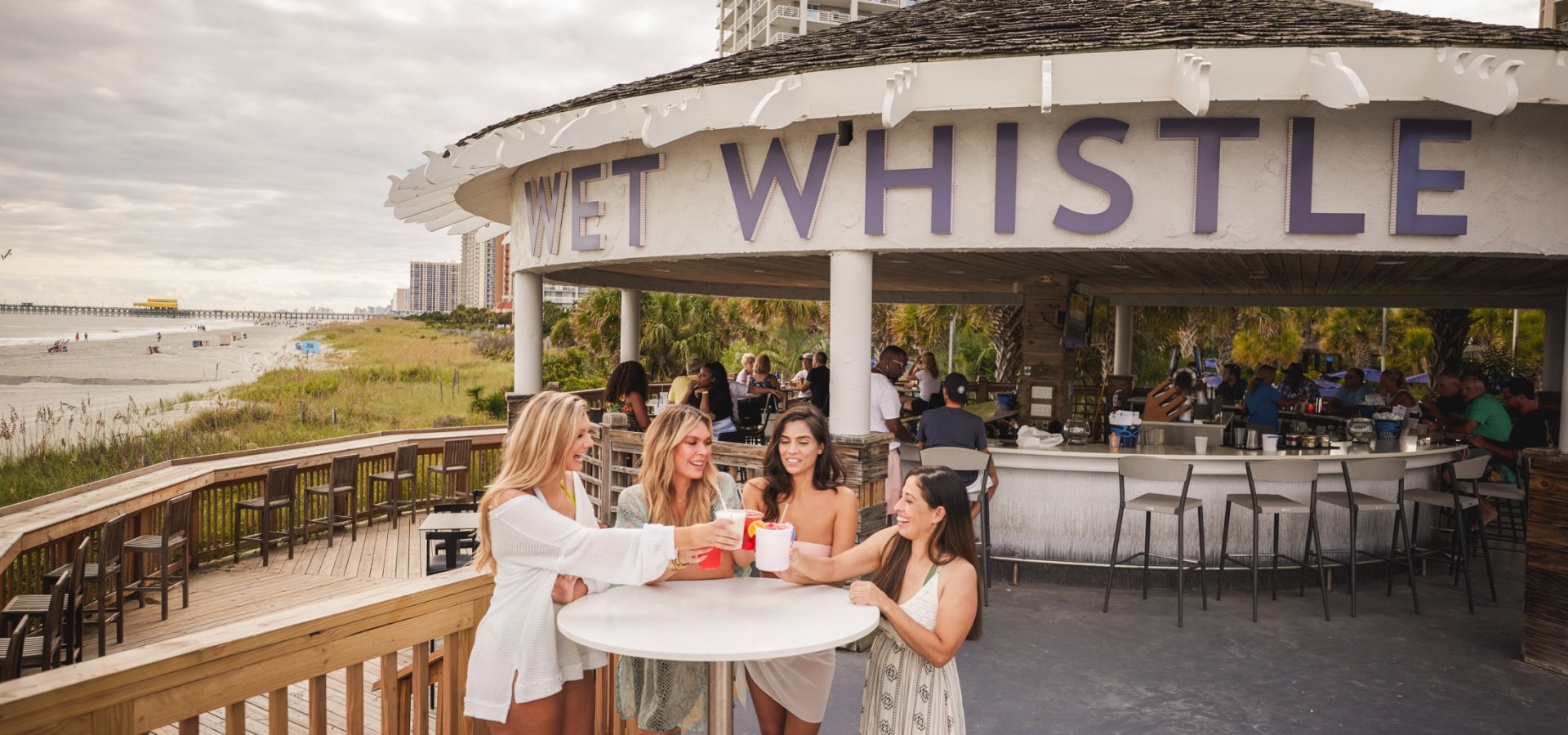 Four girls stand around a bar table cheersing drinks