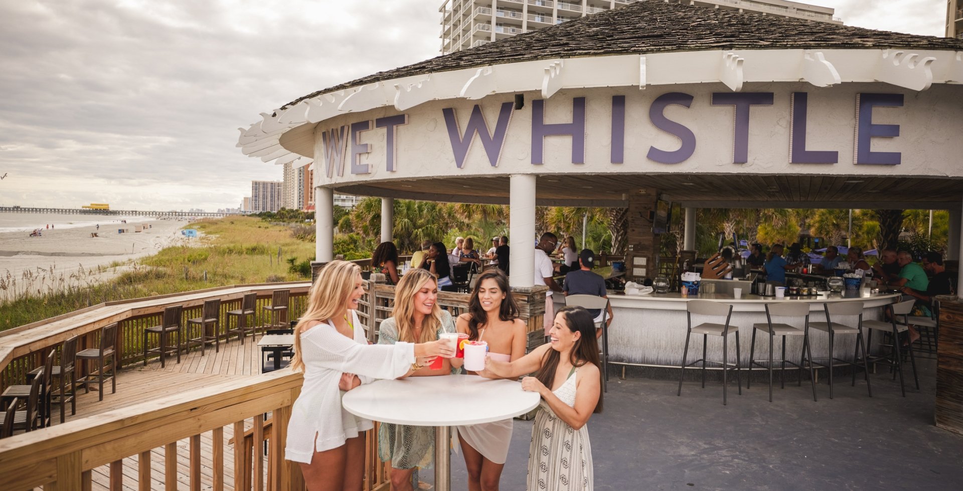 Four girls stand around a Wet Whistle bar table cheering drinks