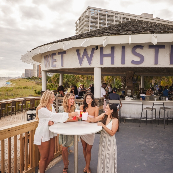 Four girls stand around a bar table cheersing drinks