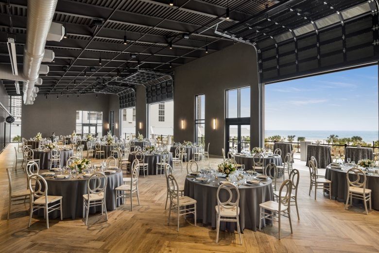 Seaside Vista set in rounds for a wedding reception. The garage doors are open with a direct view of the ocean and the terrace is set with cocktail tables