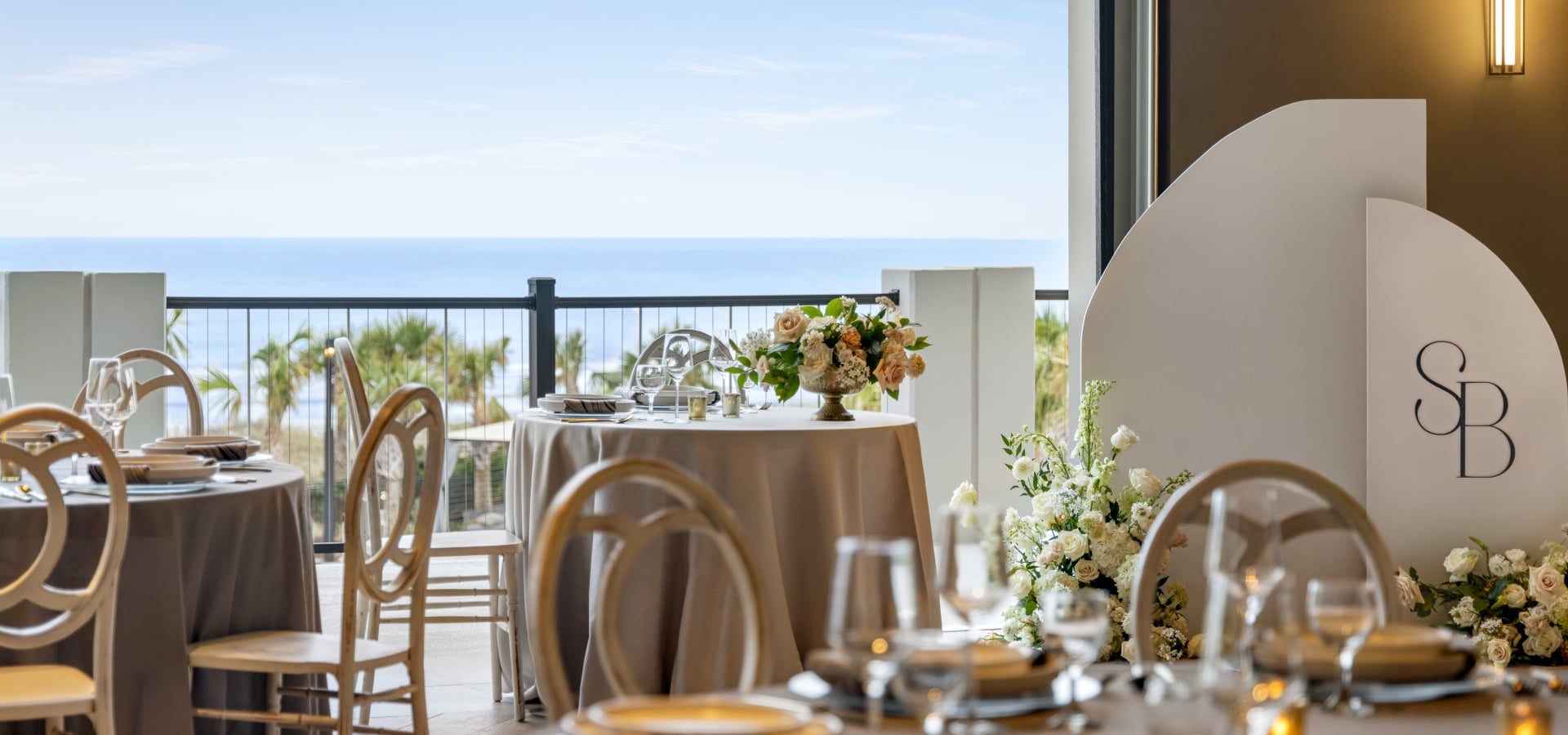 Seaside Vista ballroom set up for a wedding reception. The focus is on the bride and groom table with the ocean in the background