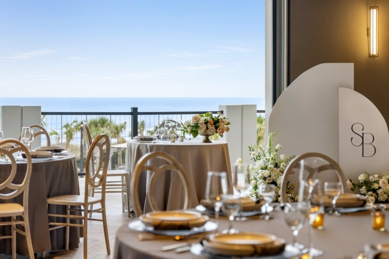 Seaside Vista ballroom set up for a wedding reception. The focus is on the bride and groom table with the ocean in the background