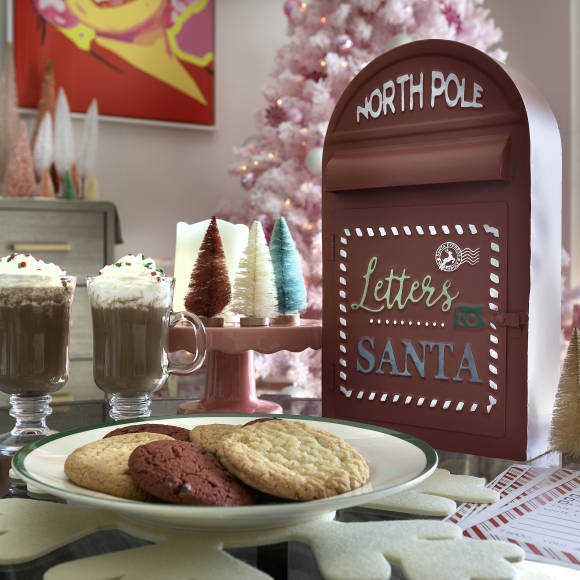 A plate of cookies and hot chocolate sits in front of a box of letters to Santa and a pink Christmas tree