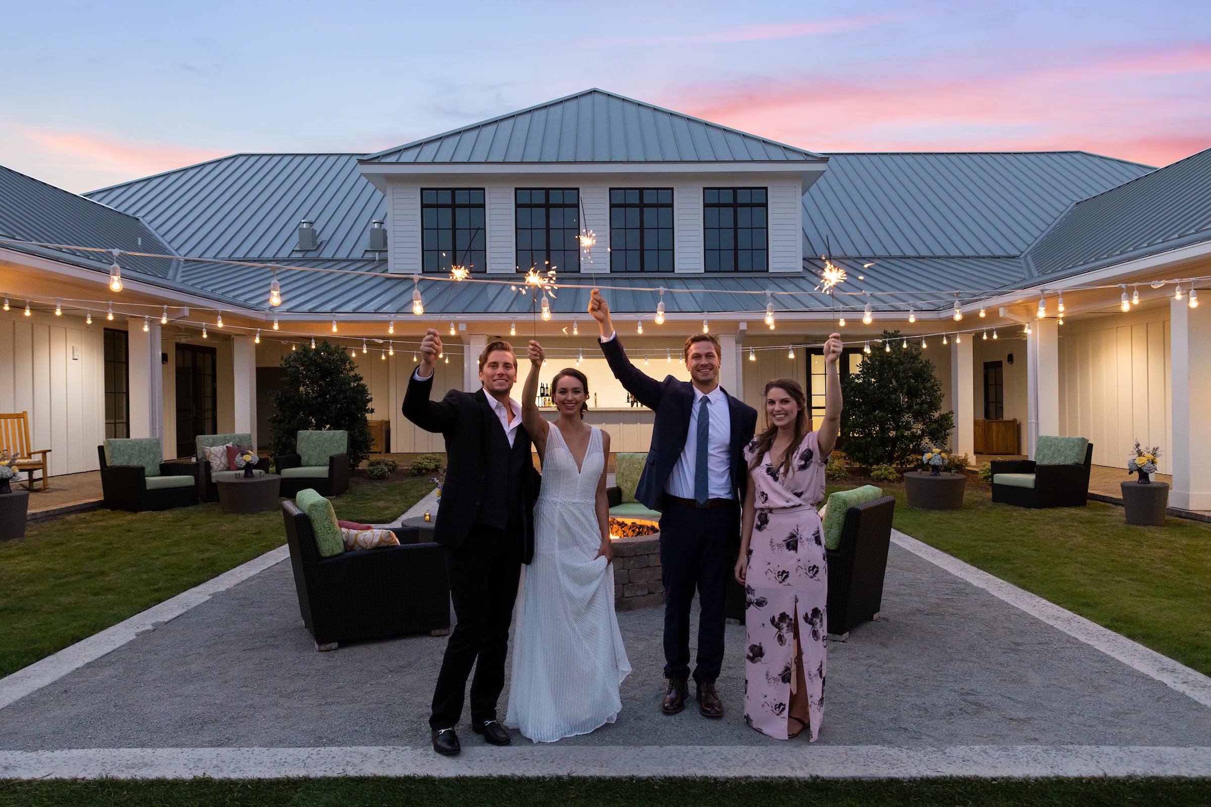 Two couples waving sparklers to the sky one in wedding attire.