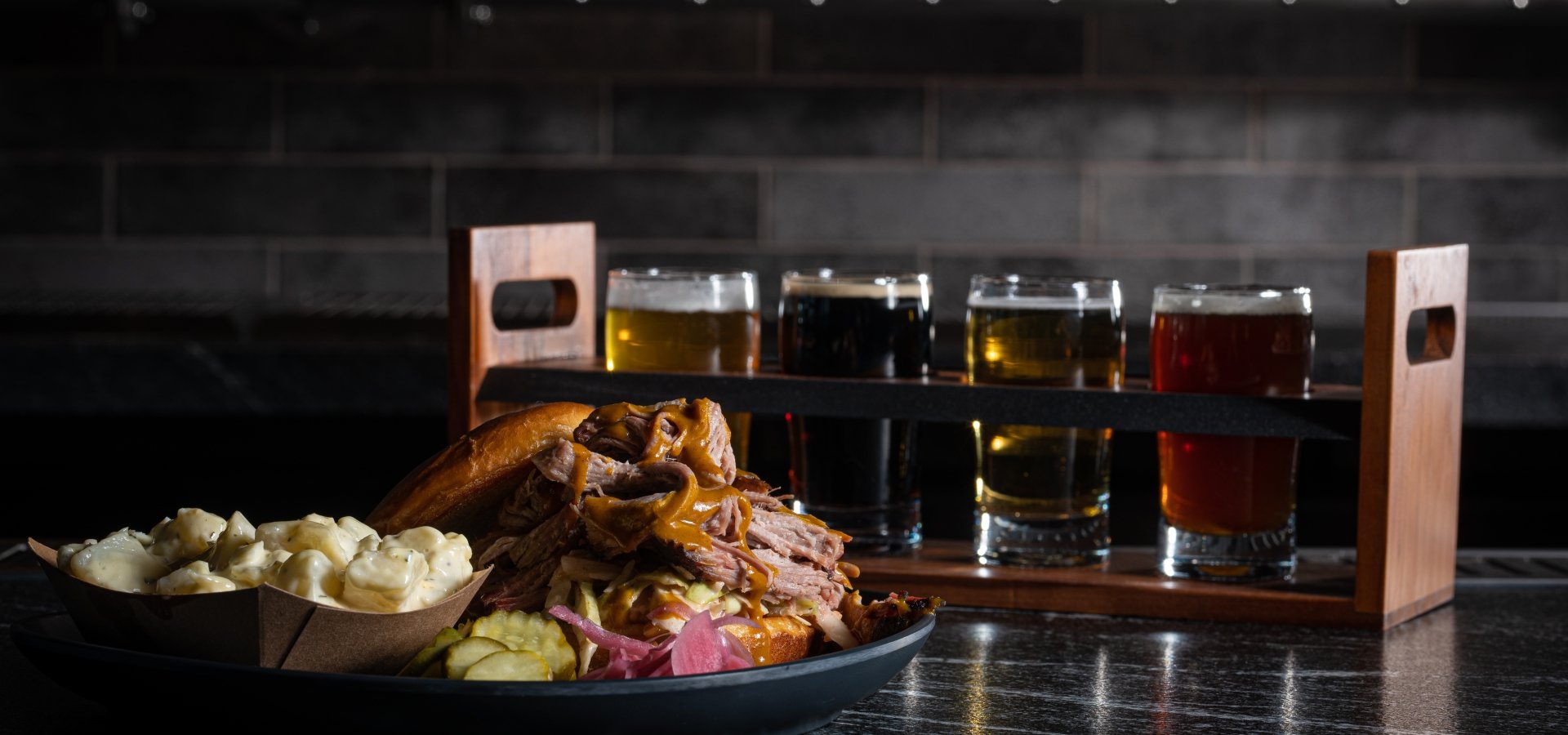 Black Drum Pulled Chicken sandwich and mac and cheese with a beer flight sitting in front of the bar