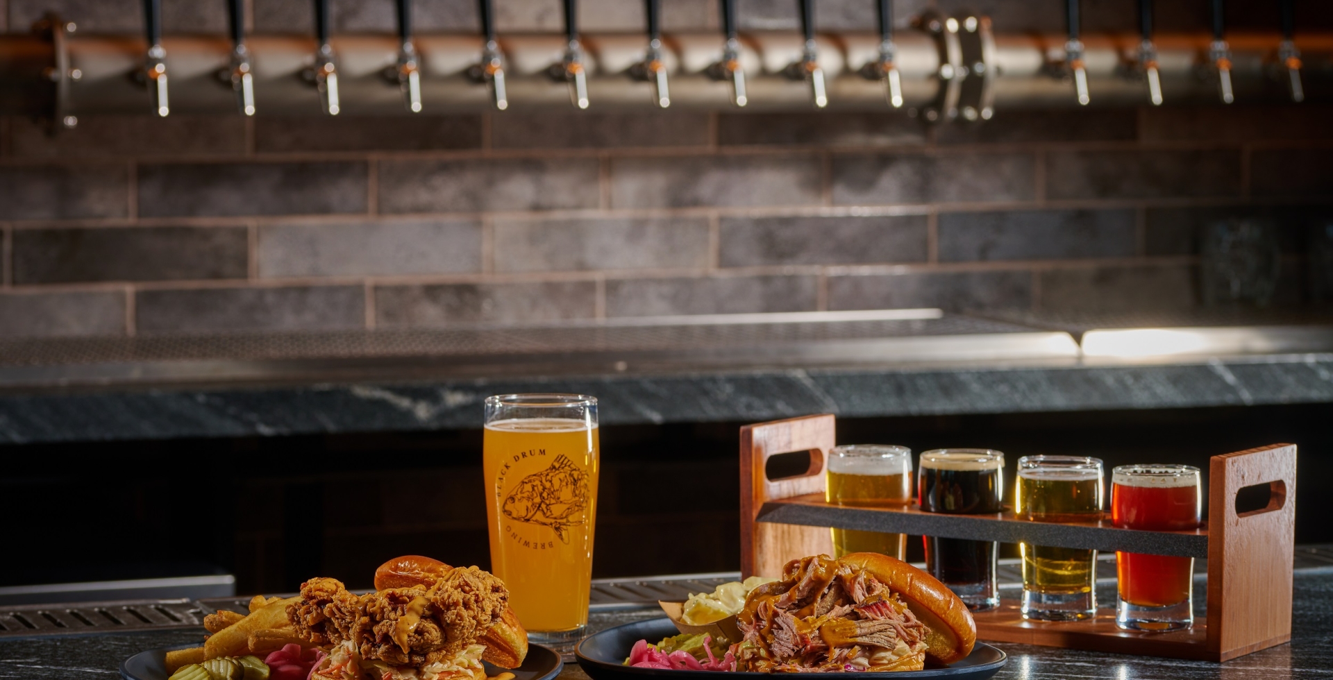 Black Drum Brewing Fried Chicken sandwich and pulled chicken sandwich with a pint of beer and a beer flight