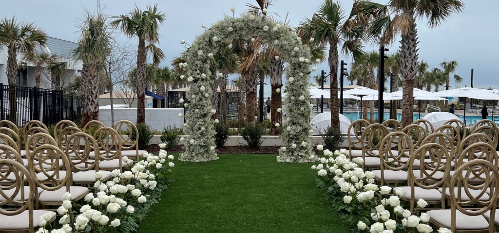 A floral arch stands between two rows of chairs on a wedding aisle.