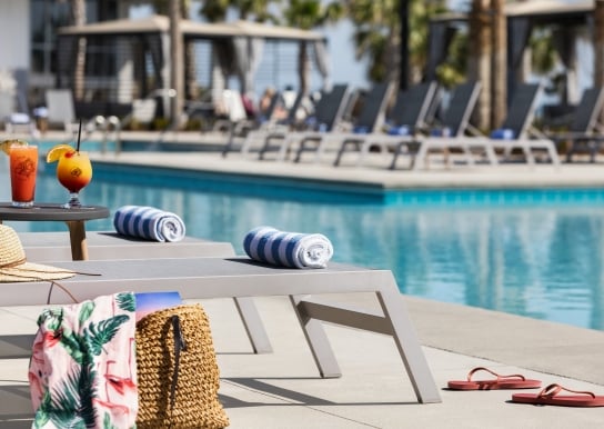 A pool char at Currents Seaside Entertainment with towels, cocktails from Black Drum Brewing, and a beach bag