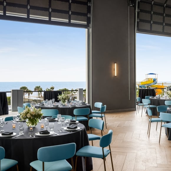Seaside Vista set in rounds for a dinner banquet. The garage doors are open to the ocean view and cocktail tables are set on the terrace