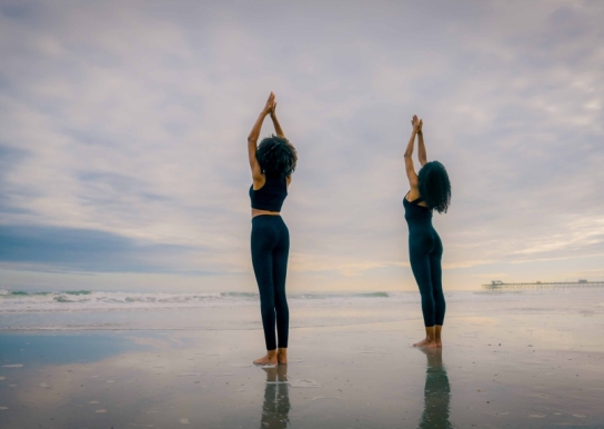Two women doing yoga on the beach