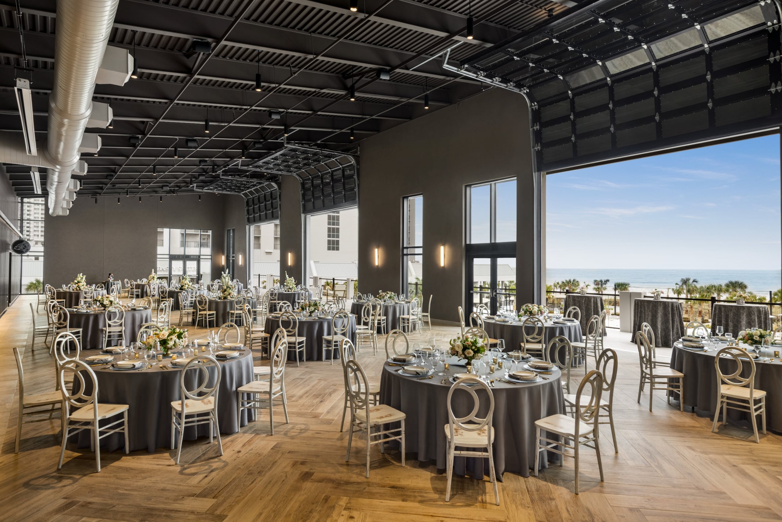 Seaside Vista set in rounds for a wedding reception. The garage doors are open with a direct view of the ocean and the terrace is set with cocktail tables