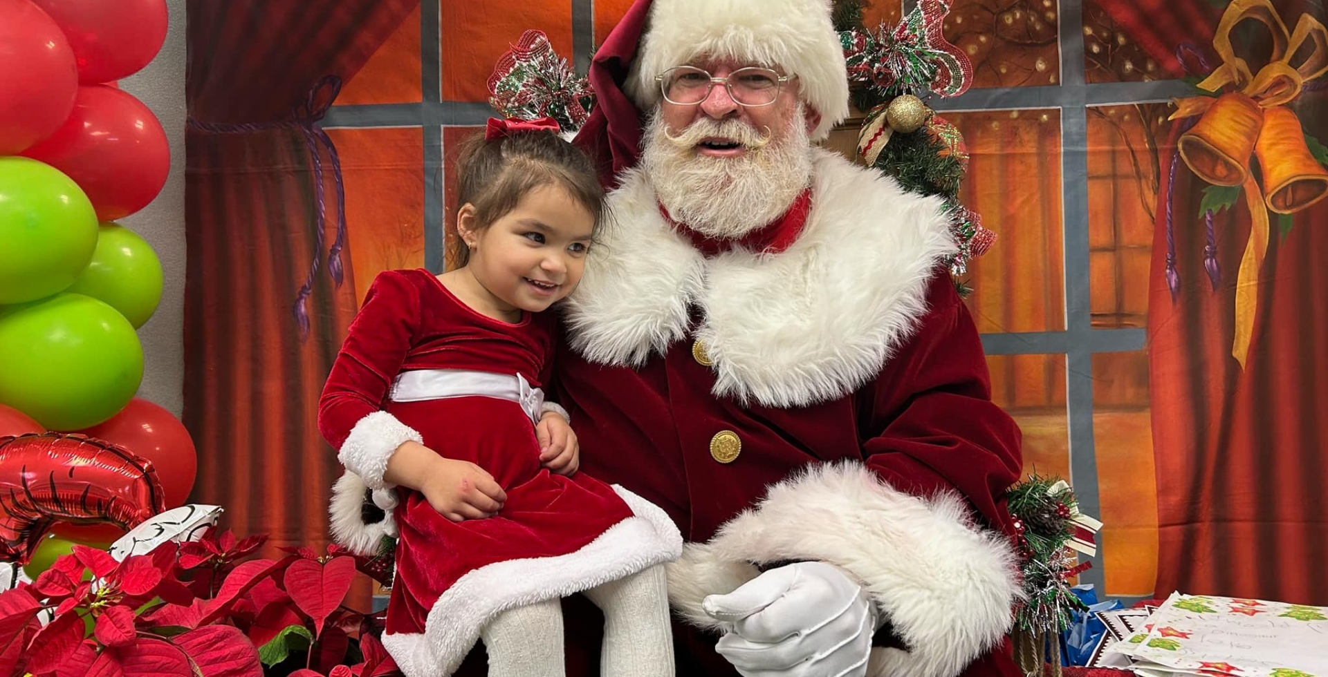 A little girl in a red and white Christmas dress sitting on Santa Clause's lap