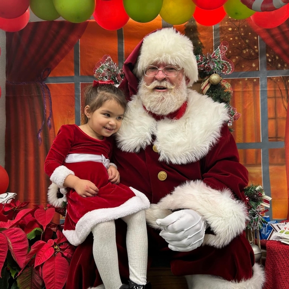 A little girl in a red and white Christmas dress sitting on Santa Clause's lap