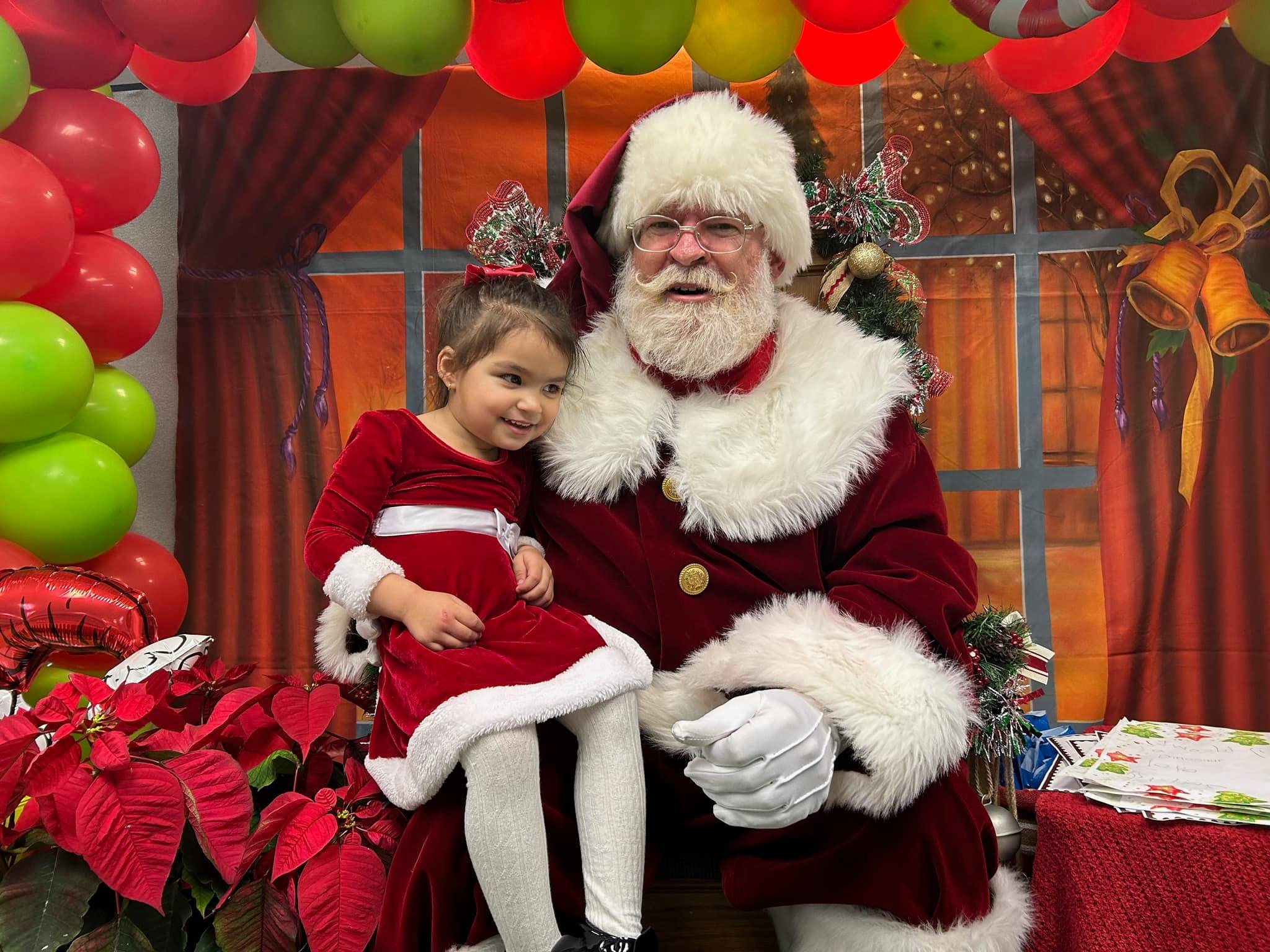 A little girl in a red and white Christmas dress sitting on Santa Clause's lap