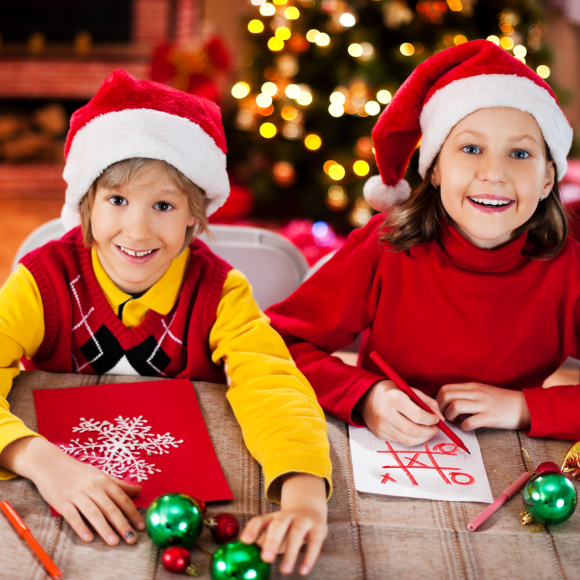 Two children with Santa hats on sitting at a table. One child is playing tic tac toe and the other has a snowflake on his paper