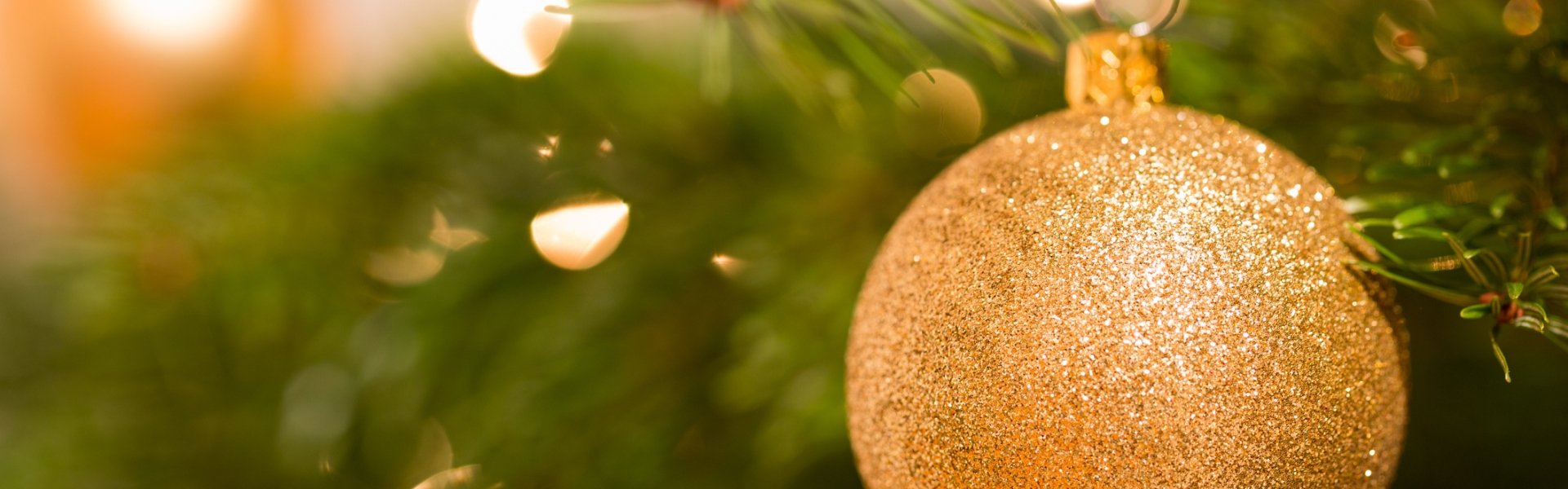 A glittery gold Christmas ornament hanging on a Christmas tree branch