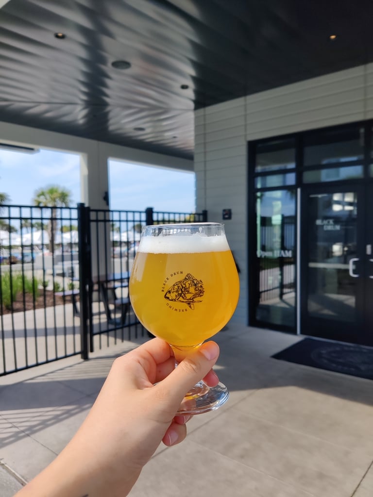 A hand holds a glass of beer in the air.
