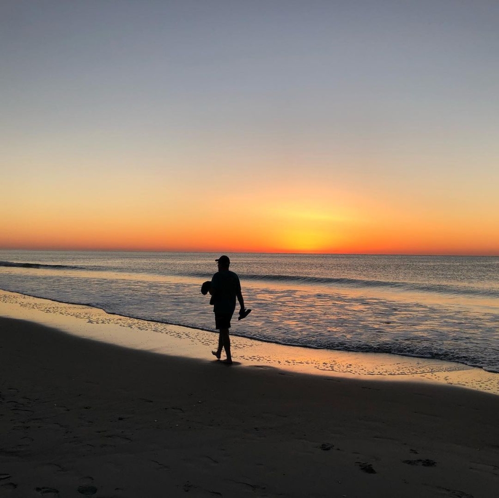 A silhouette of a person walking on the beach at sunrise.