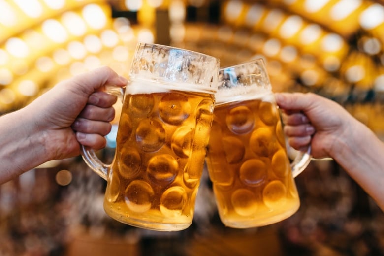 Two people cheering two beers in front an arch of lights