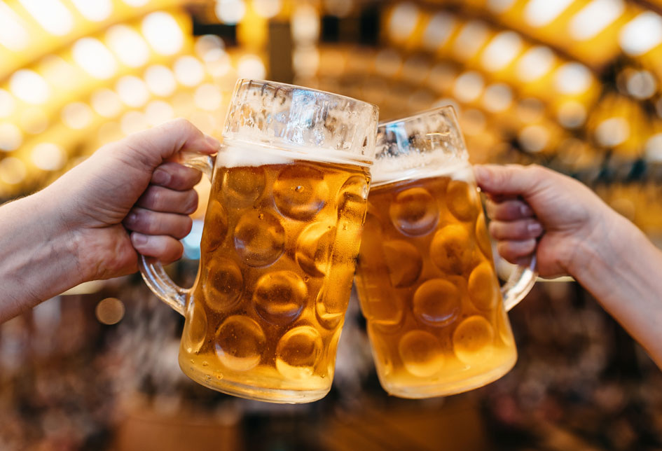 Two people cheering two beers in front an arch of lights