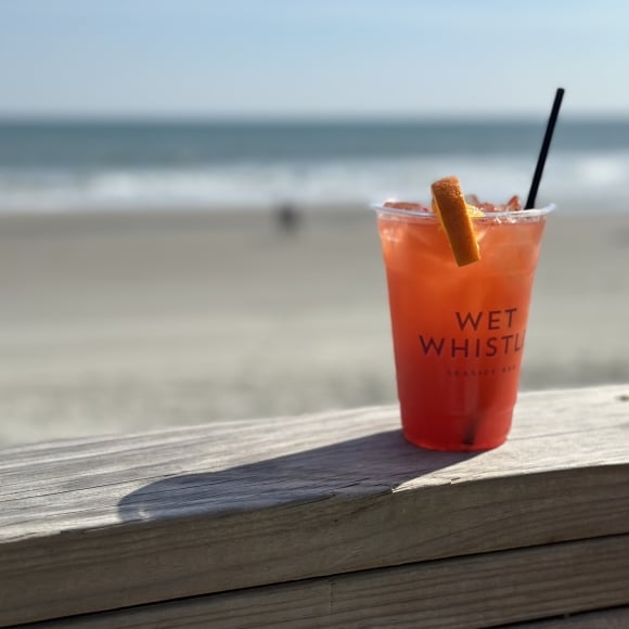 A orange colored drink sits on a ledge with the beach in the background,