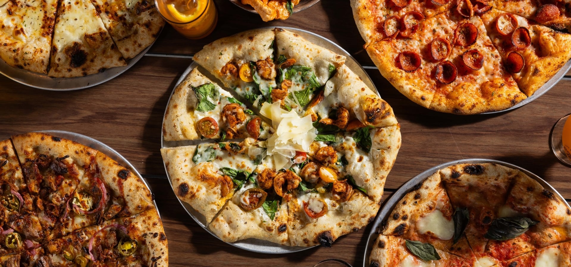 5 different Black Drum Brewing pizzas, pork skins, wings, and drinks on the table