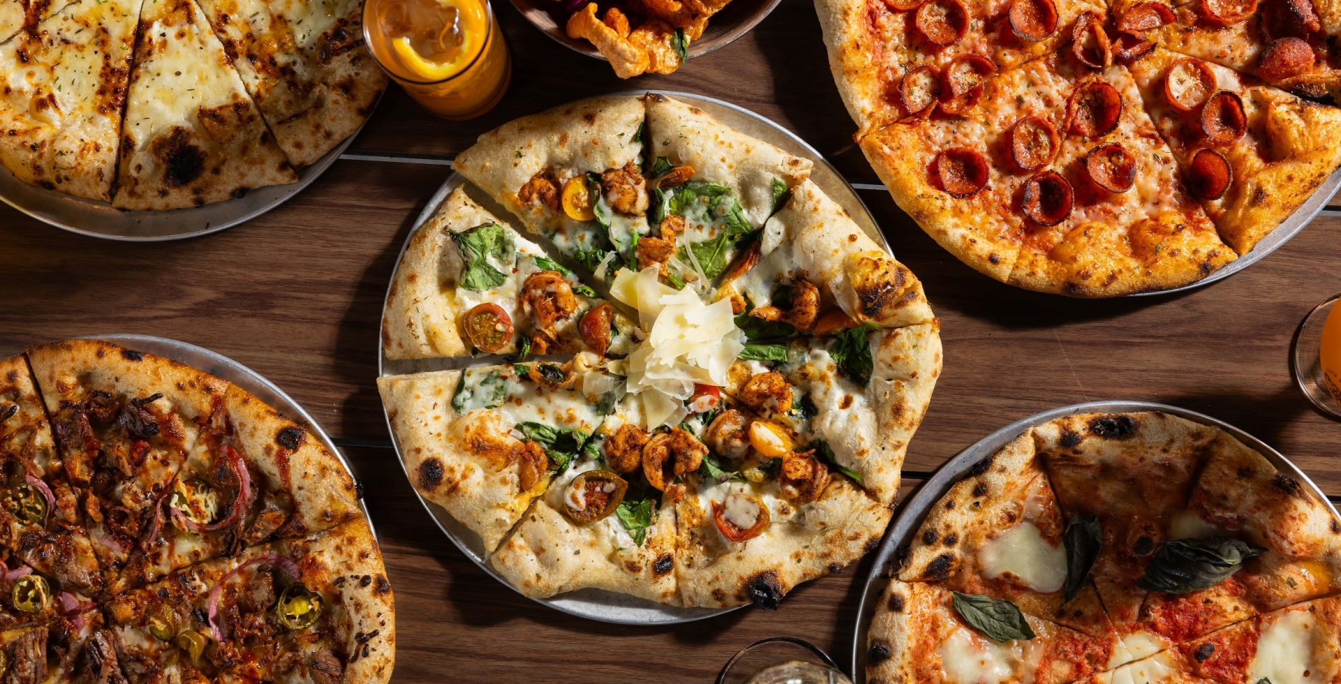 5 different Black Drum Brewing pizzas, pork skins, wings, and drinks on the table