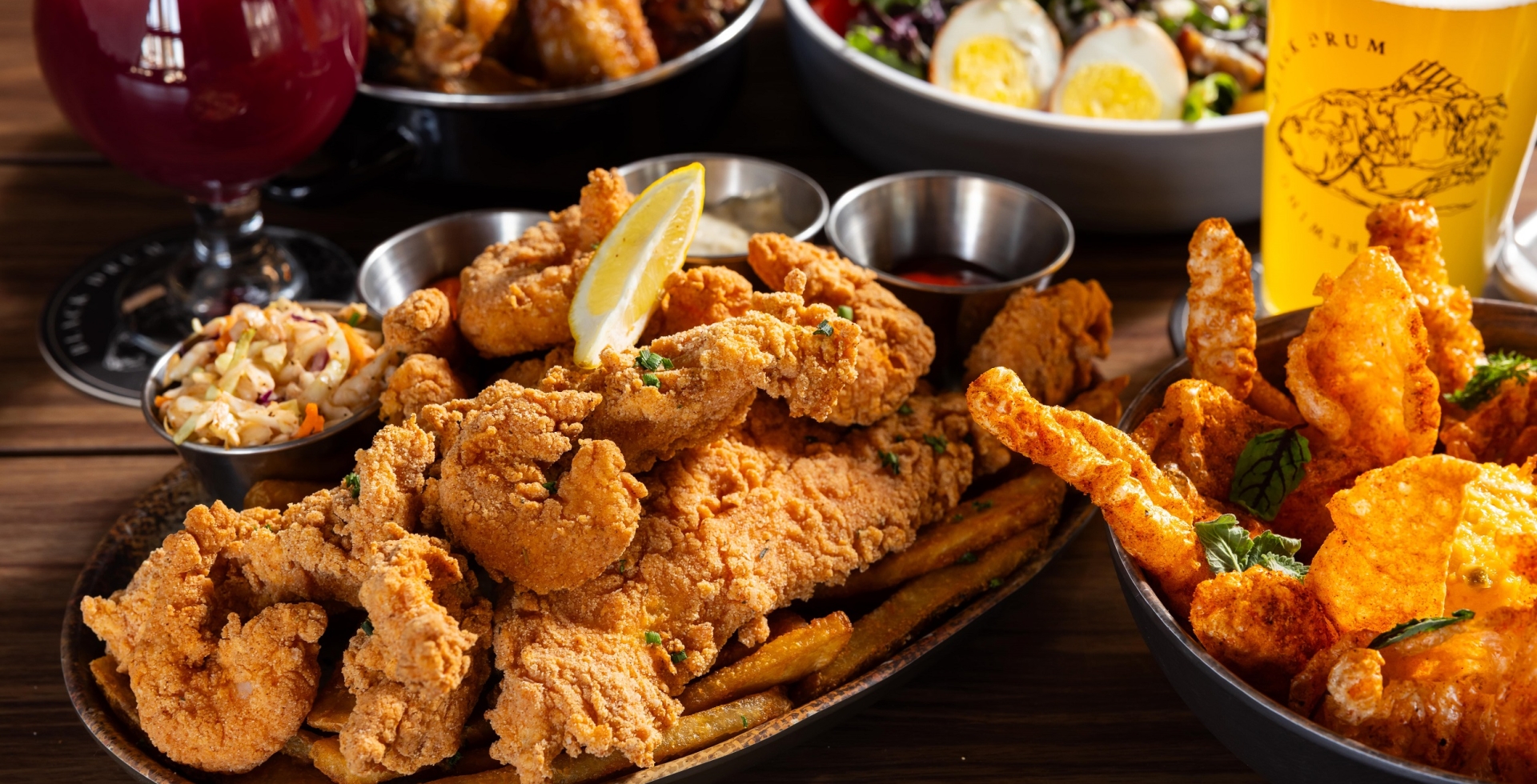 Black Drum Brewing spread of food including the shrimp & fish platter, pork skins, a cobb salad, wings, and beer