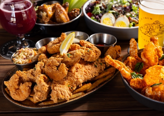 Black Drum Brewing spread of food including the shrimp & fish platter, pork skins, a cobb salad, wings, and beer